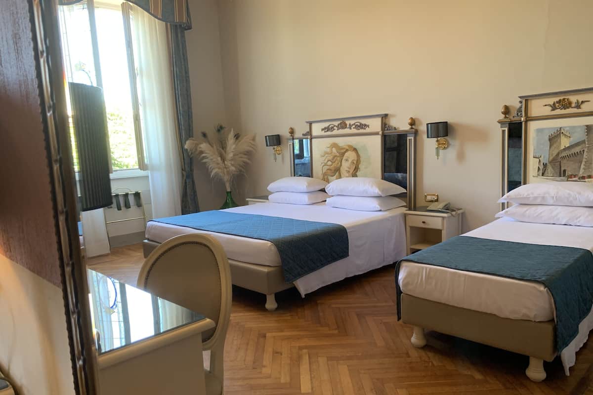 A hotel room with two beds, a wooden herringbone floor, a desk, and a chair.