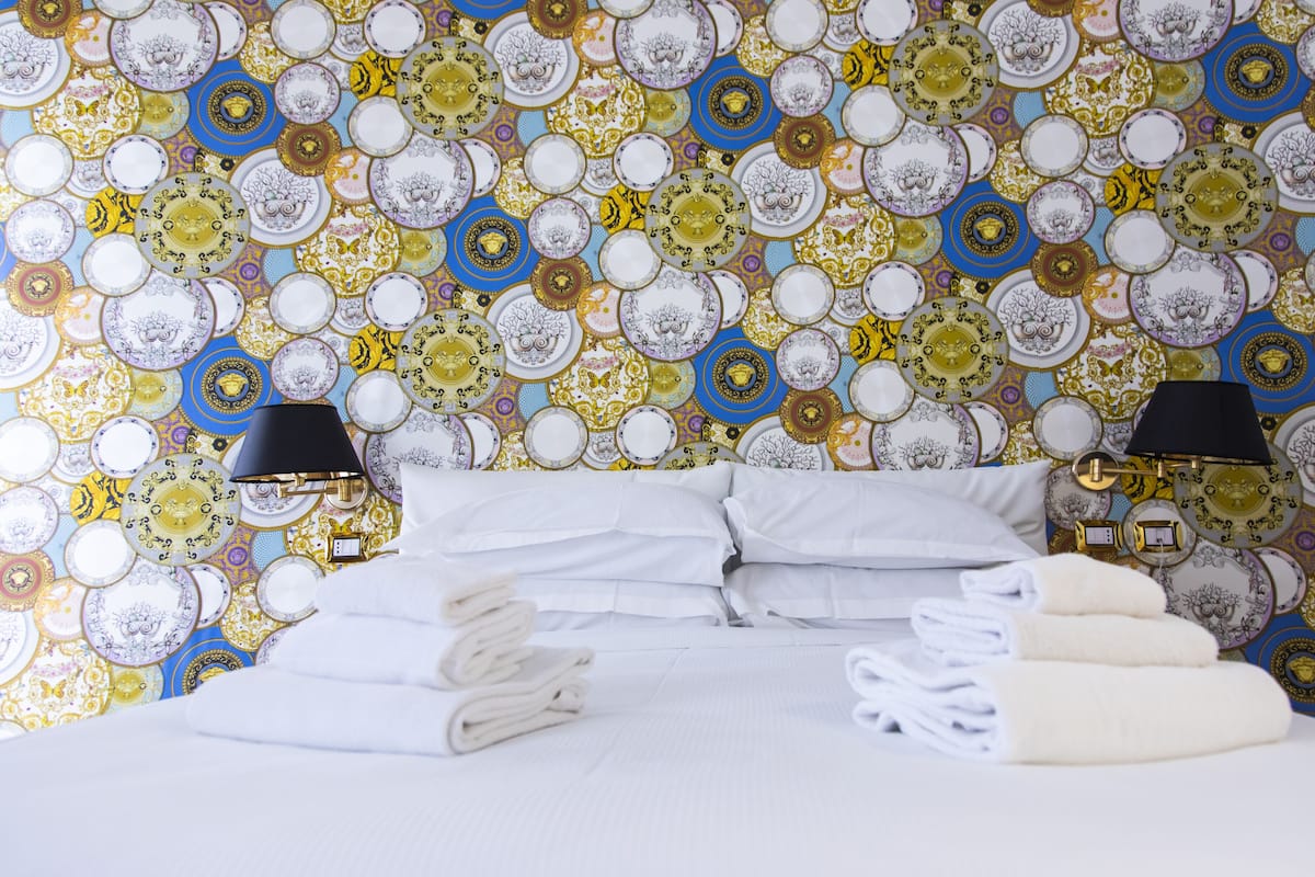 A hotel room with a bed, white linens, two black lamps, and a wall covered with patterned plates.