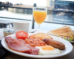 A breakfast plate with bacon, eggs, beans, toast, and a glass of orange juice.