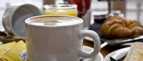 A white coffee cup on a saucer, a croissant, a glass of orange juice, and a packet of sugar on a table.