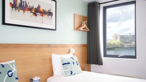 Quarto de hotel com duas camas, uma pintura de paisagem urbana, vista de um edifício através de um rio e uma janela com cortinas.
