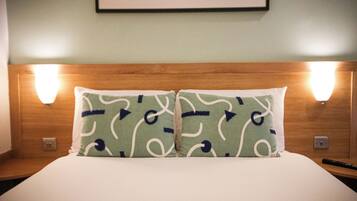 A neatly made bed with two pillows, a wooden headboard, and two wall-mounted lights.