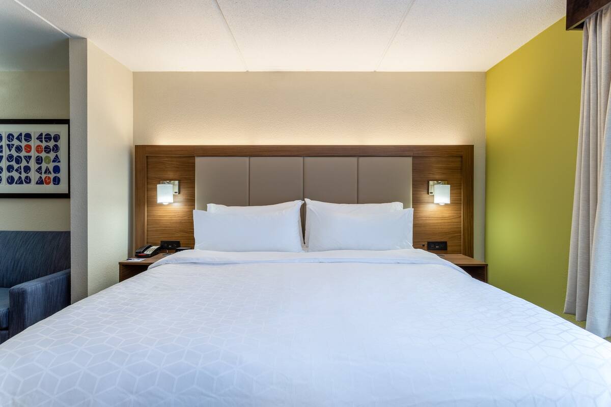 A hotel room with a large bed, two bedside tables with lamps, a headboard with built-in lighting, and a wall-mounted artwork.