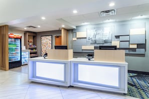 A hotel reception area with a Coca-Cola refrigerator, a digital kiosk, and a wall-mounted sign for Holiday Inn Express & Suites. - Holiday Inn Express & Suites Cedar Falls - Waterloo by IHG (Cedar Falls)