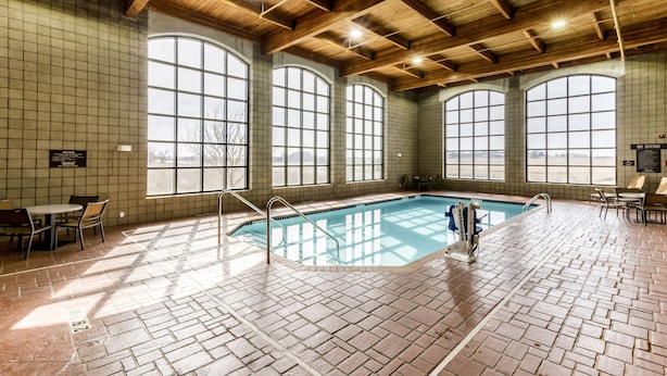 An indoor swimming pool with a tiled floor, large arched windows, and wooden ceiling beams.