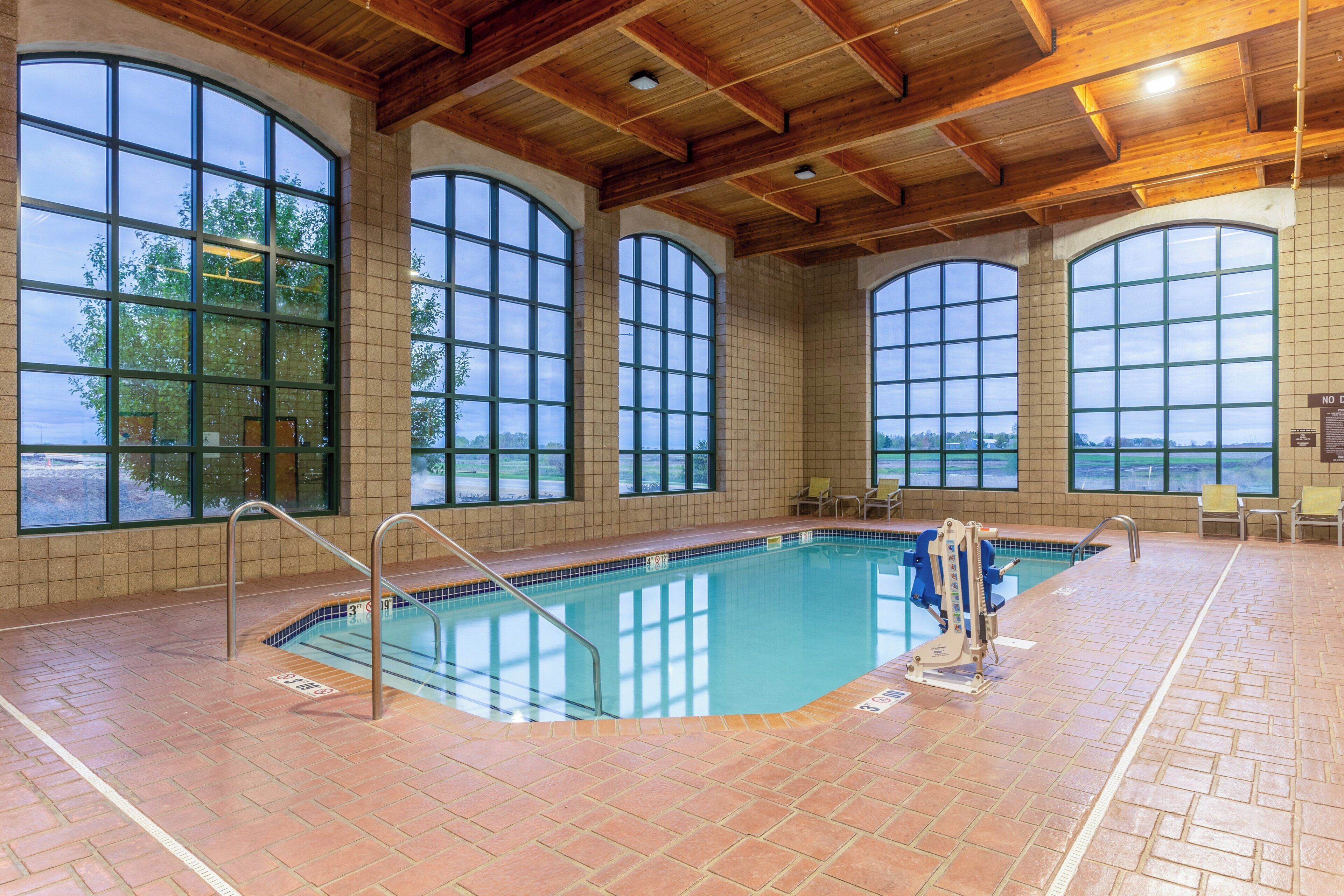 An indoor swimming pool with large windows, a wooden ceiling, and a tiled floor.