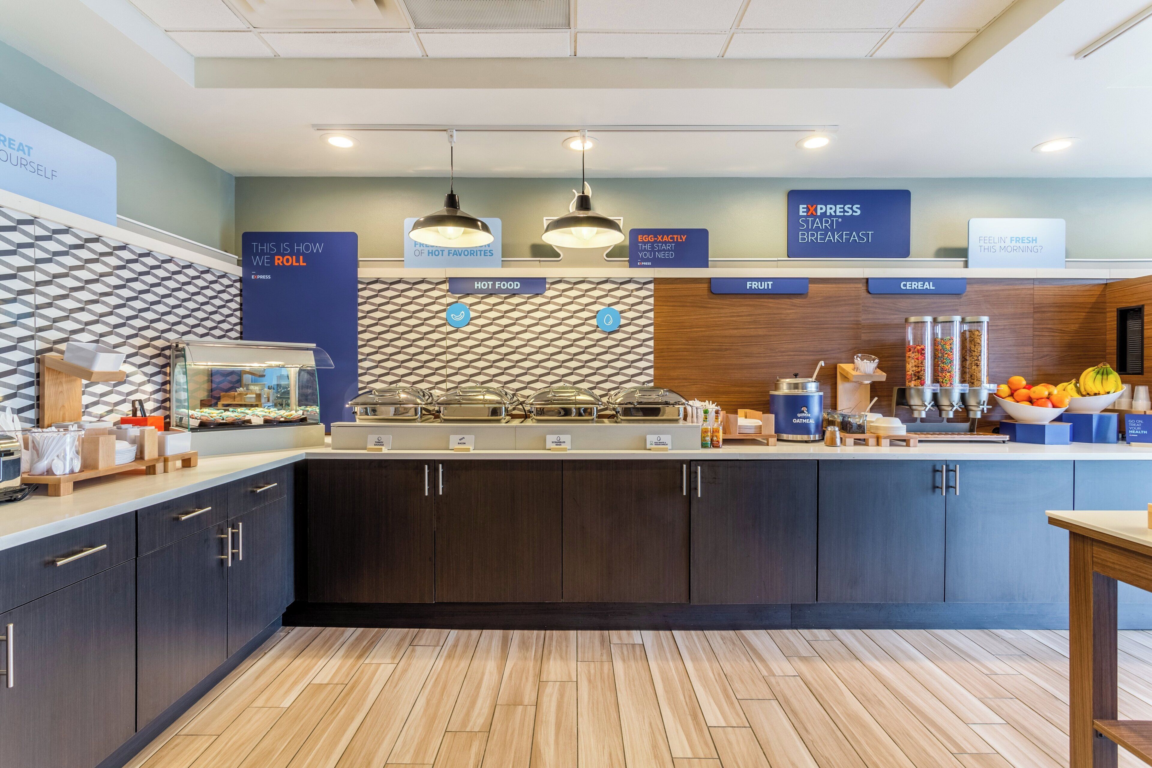 A breakfast area with labeled sections for hot food, fruit, and cereal, and a sign indicating the start of breakfast.