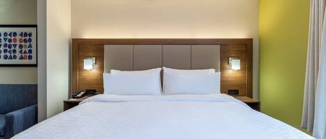 A hotel room with a large bed, two bedside tables, a headboard with built-in lighting, and a framed picture on the wall.