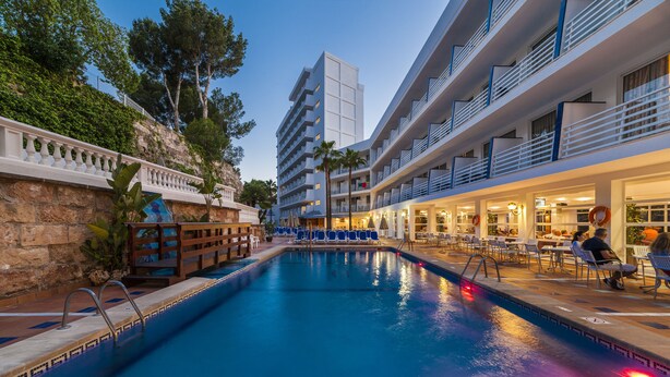 Zona de piscina con vista despejada, sillas de descanso y un edificio con balcones.