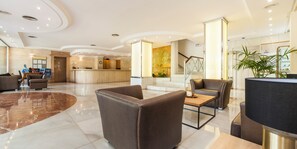 Un vestíbulo de hotel con una recepción, zona de estar y una escalera.