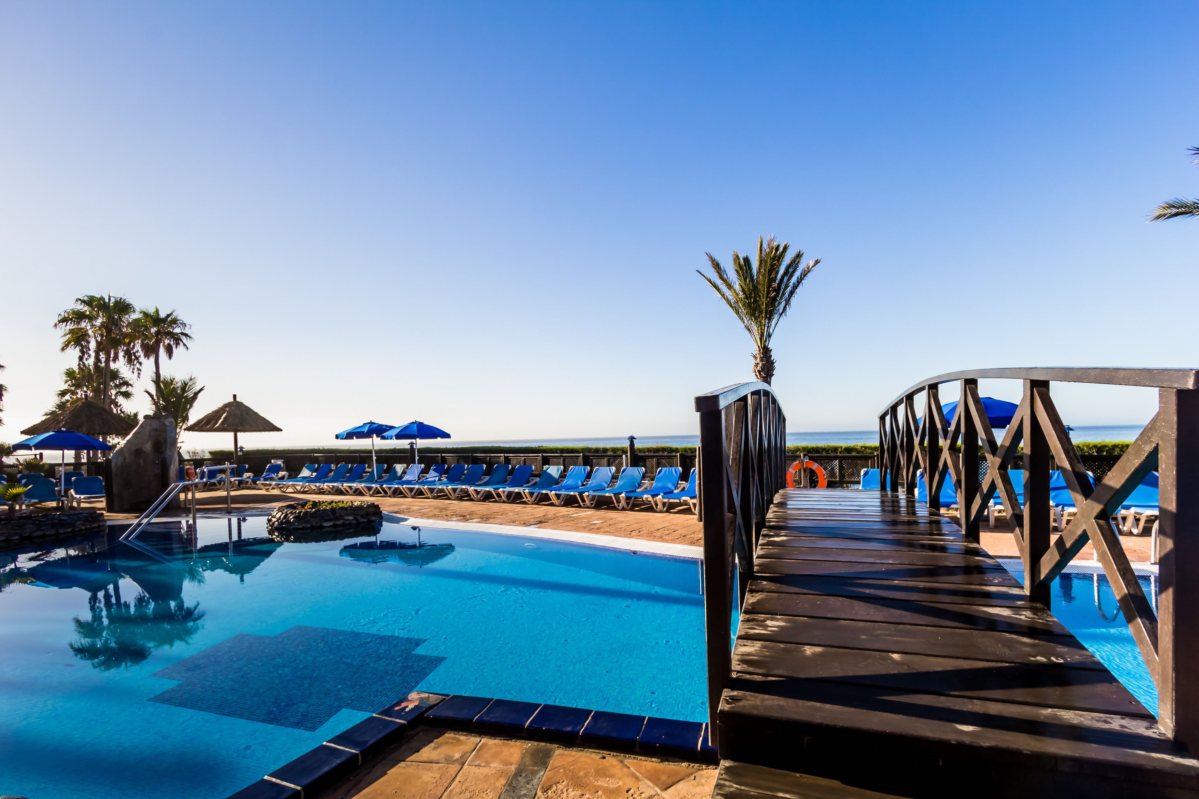 A pool area with lounge chairs and umbrellas, a wooden deck, and a clear sky.