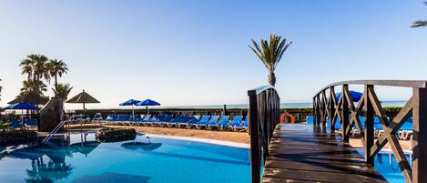 A pool area with lounge chairs and umbrellas, a wooden deck, and a clear sky.