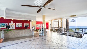 A hotel lobby with a reception desk, artwork, a large fan, and a view of the ocean. - BlueBay Beach Club Aparthotel (San Bartolomé de Tirajana)