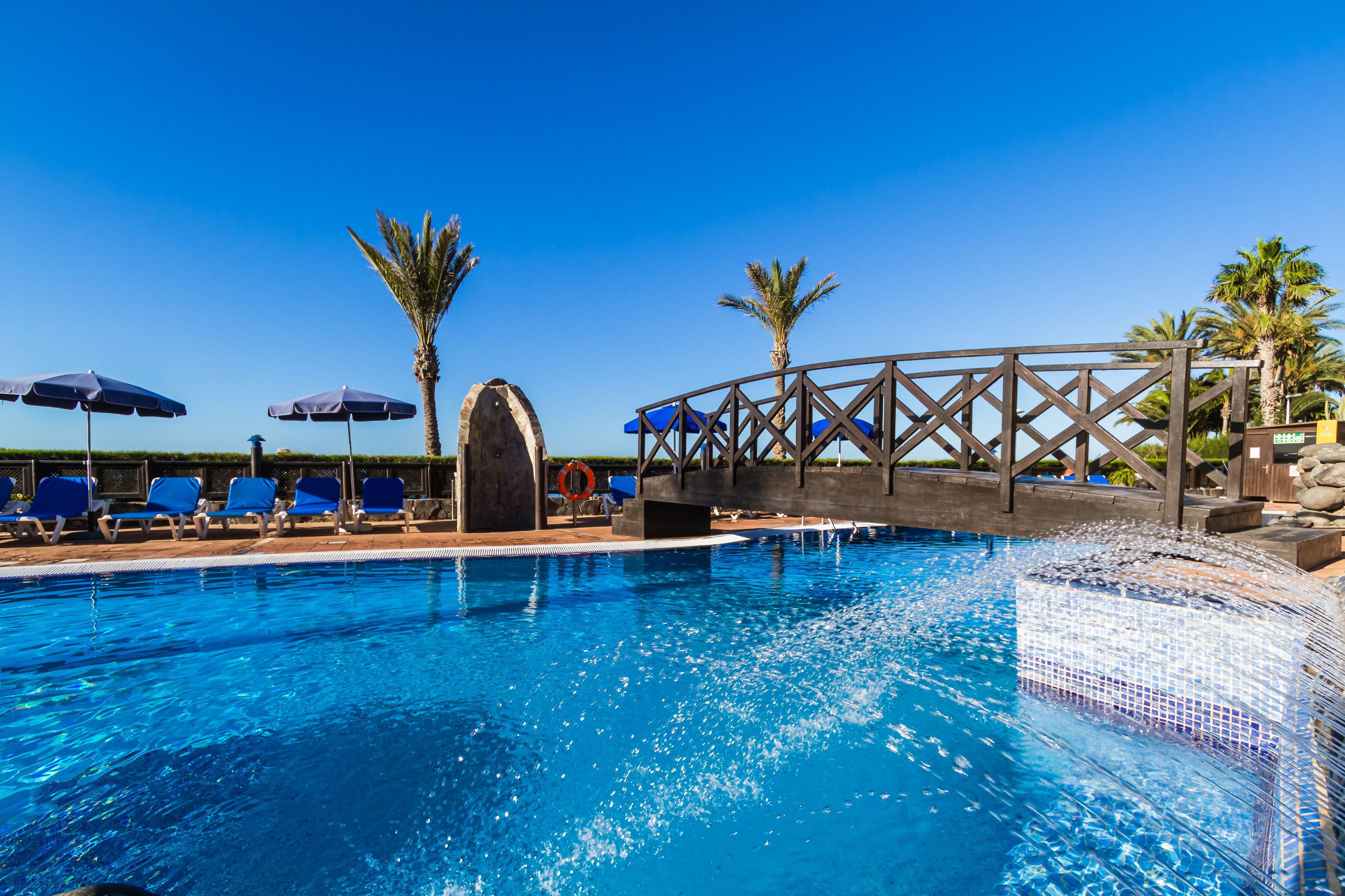 Zwembad met blauw water, omringd door ligbedden en parasols.