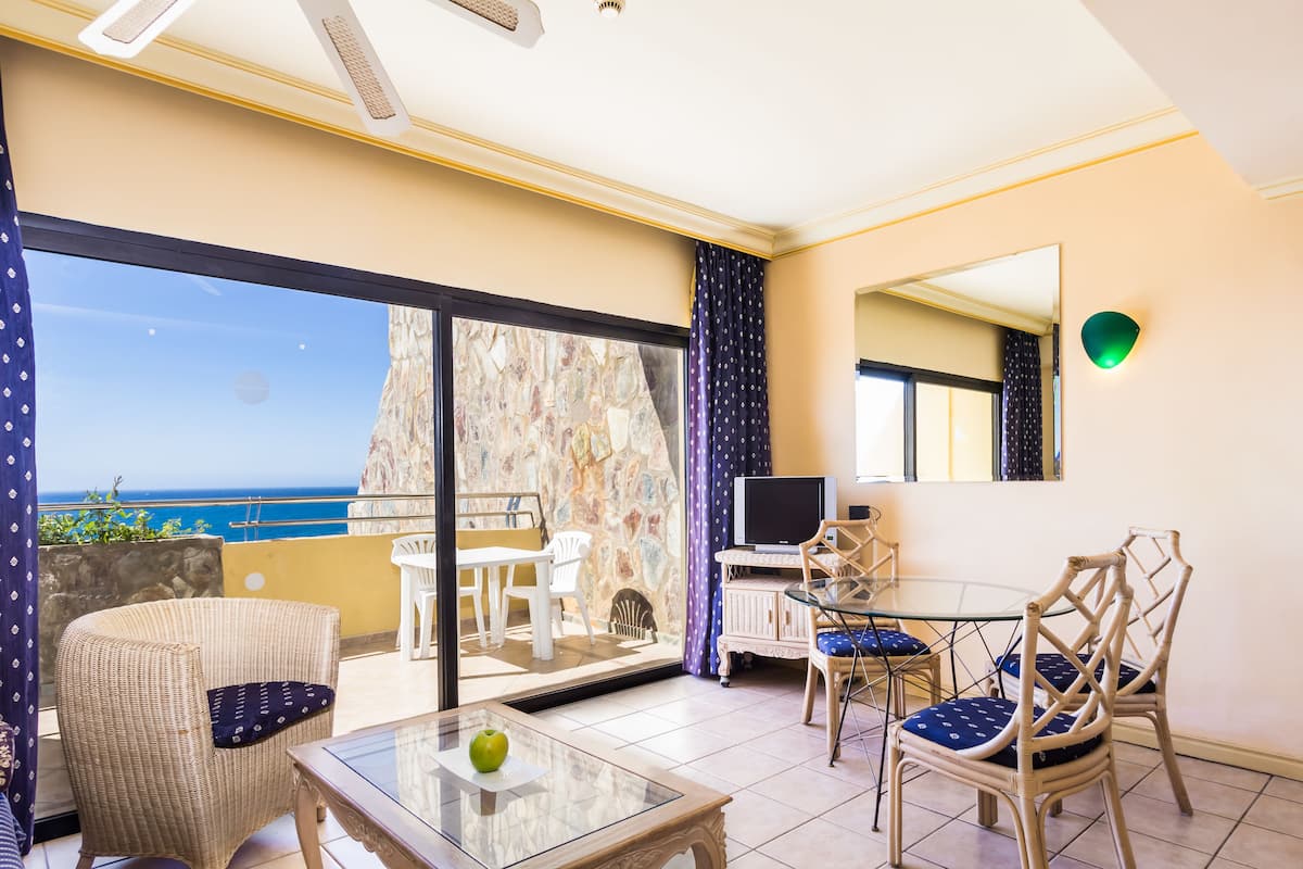 A balcony with a view of the ocean, a dining area with chairs and a table, and a television on a stand.