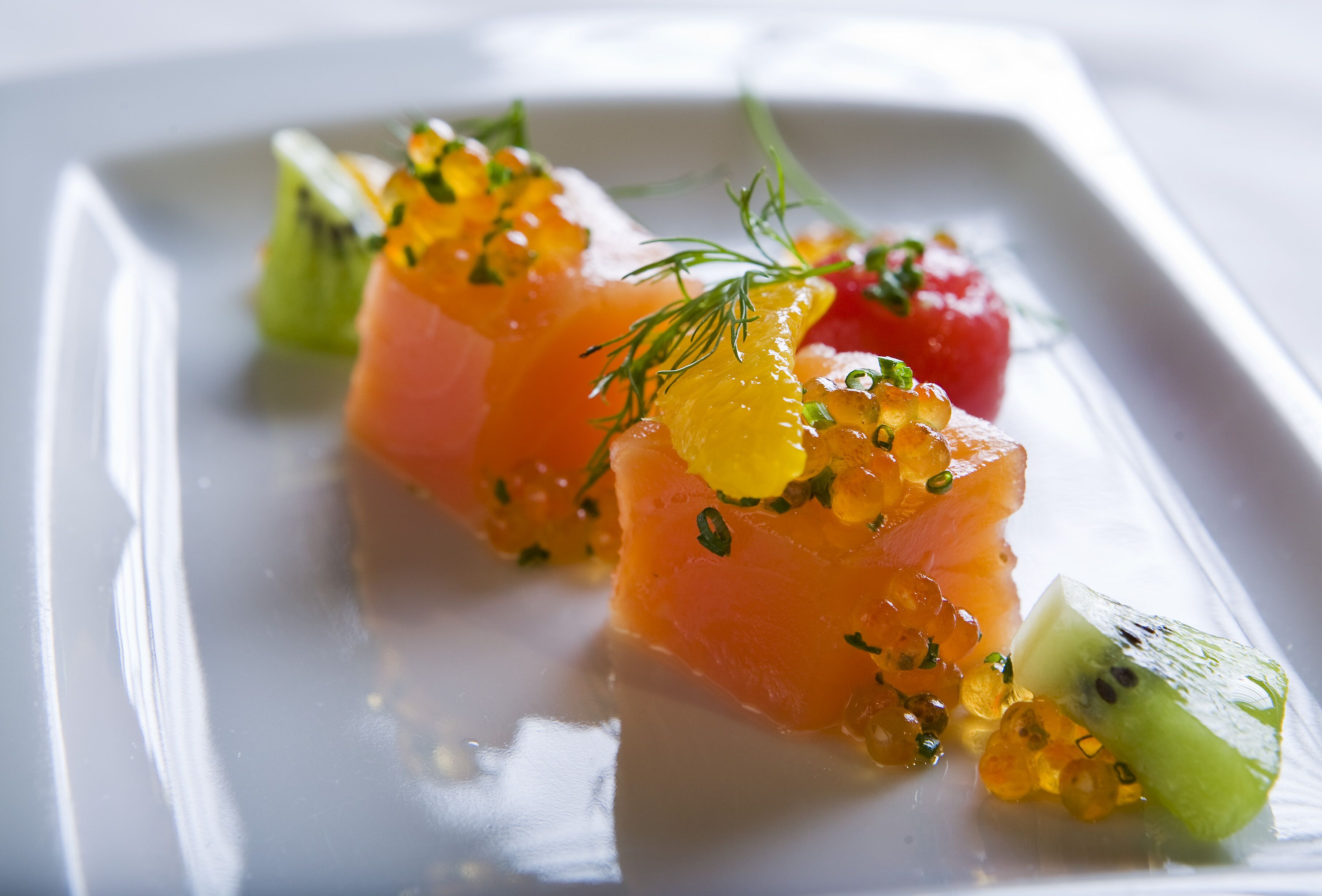 Une assiette rectangulaire blanche sur laquelle sont disposés du saumon, du caviar et quelques herbes en guise de décoration.
