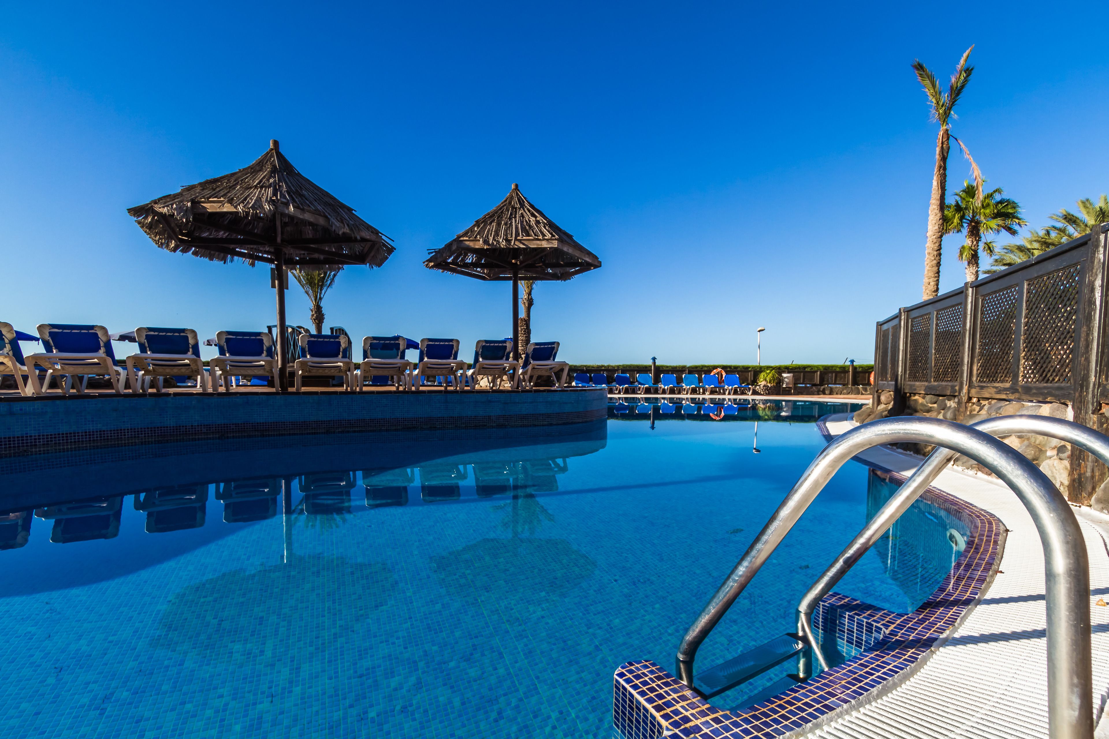 Une piscine dotée de chaises longues et de parasols en chaume.
