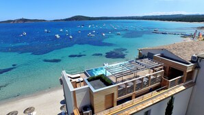 A rooftop pool with clear blue water, a view of the sea with boats, and a beach in the background. - Hotel Le Pinarello (Zonza)