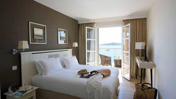 A hotel room with a bed, bedside table, lamp, and a view of the sea.