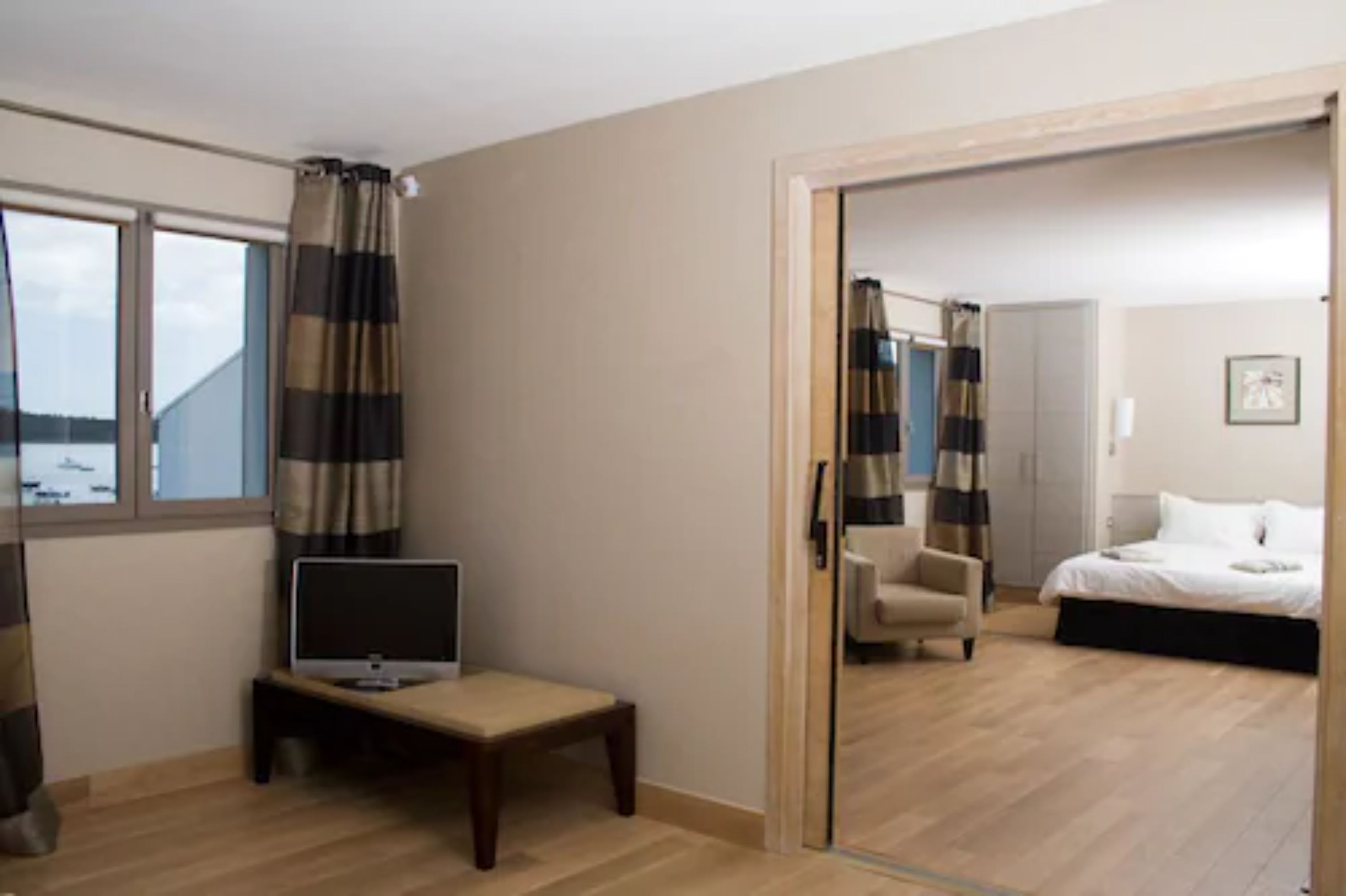 A hotel room with a bed, a chair, a TV on a small table, and a view of the outdoors through a window.