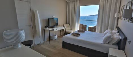 Ein Hotelzimmer mit Bett, Schreibtisch mit Fernseher, Stuhl, Meerblick und Balkon mit Korbmöbeln.