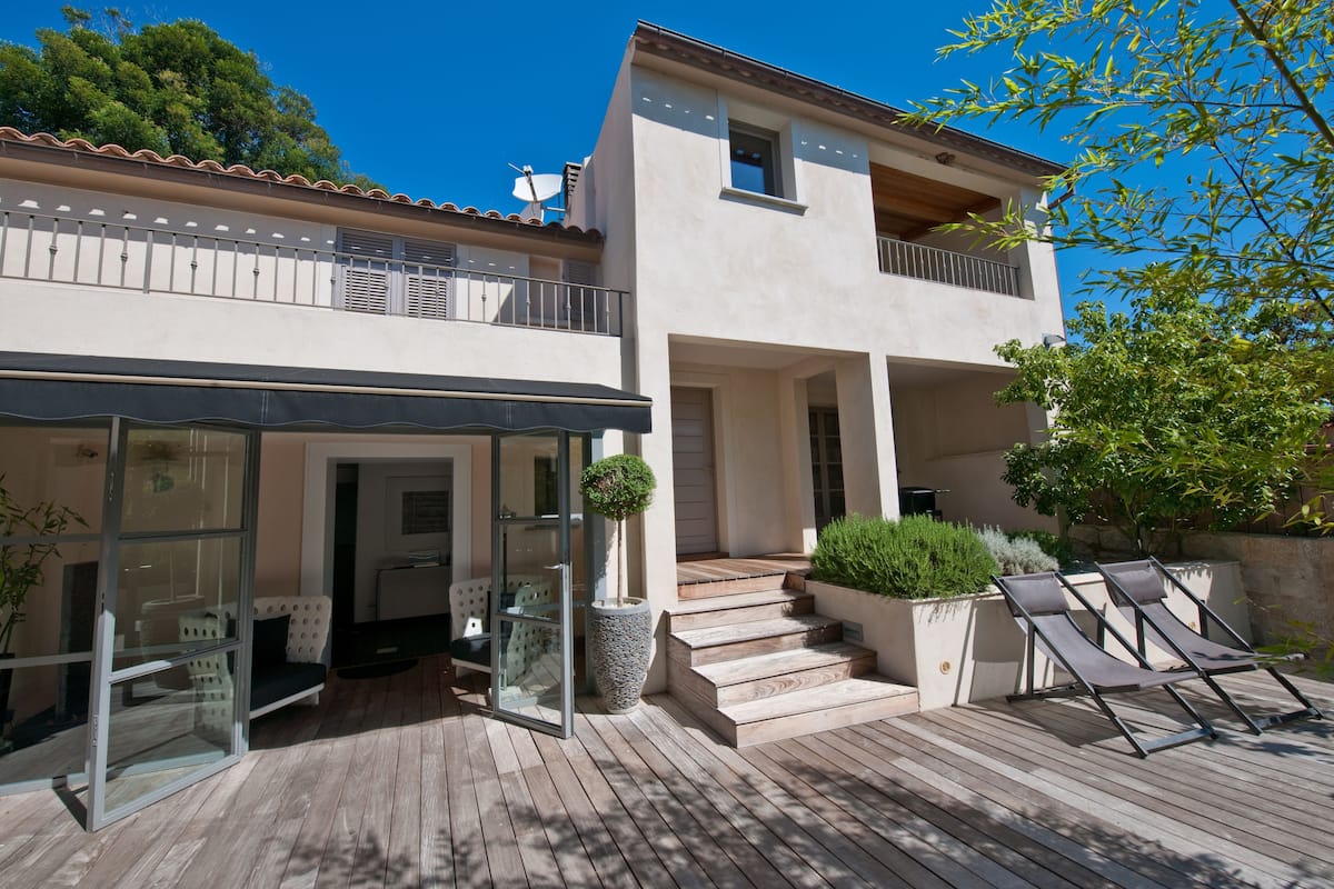 A modern two-story house with a wooden deck, outdoor seating, and a satellite dish.