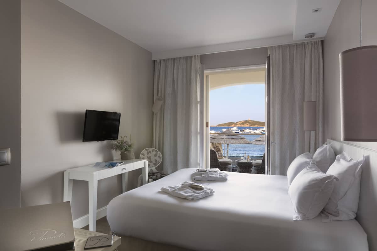 A hotel room with a bed, a desk, a TV, and a view of the sea.