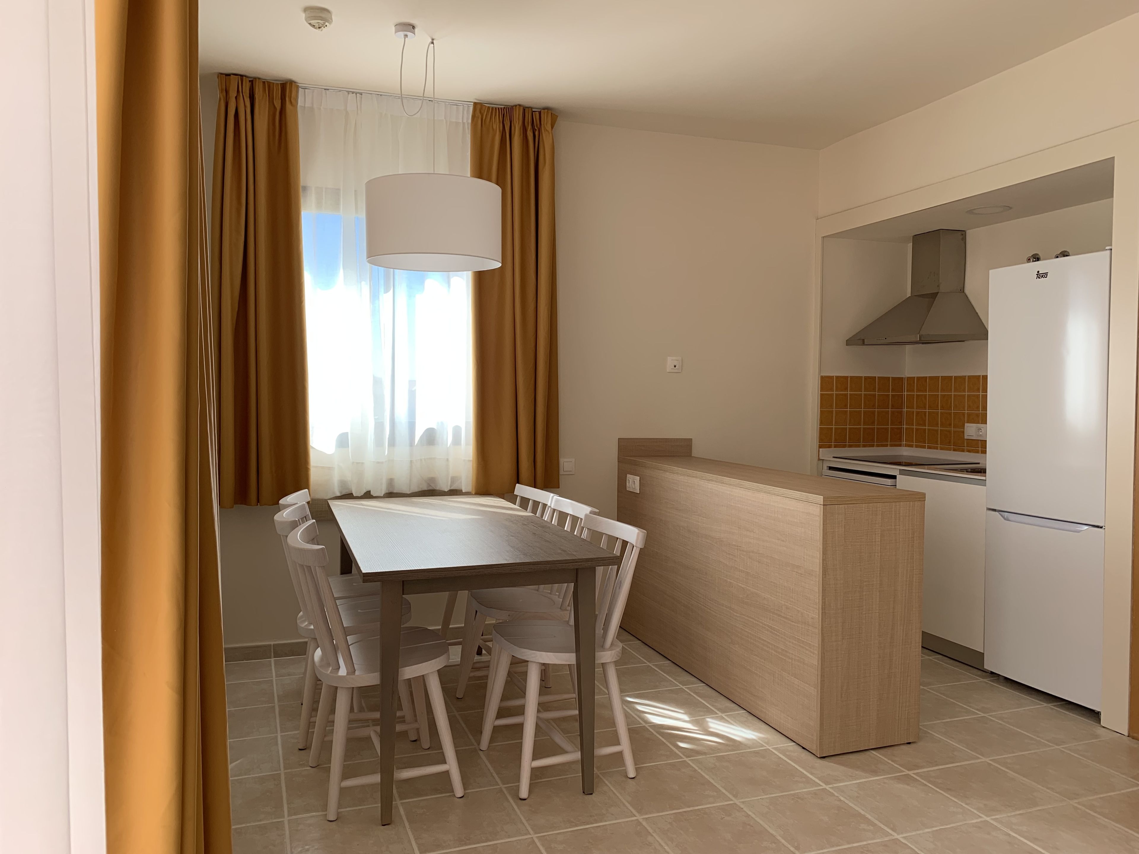 Cocina compacta con zona de comedor, que incluye una mesa blanca, sillas y una pequeña isla con horno integrado.