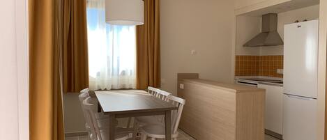 Cocina compacta con zona de comedor, que incluye una mesa blanca, sillas y una pequeña isla con horno integrado.