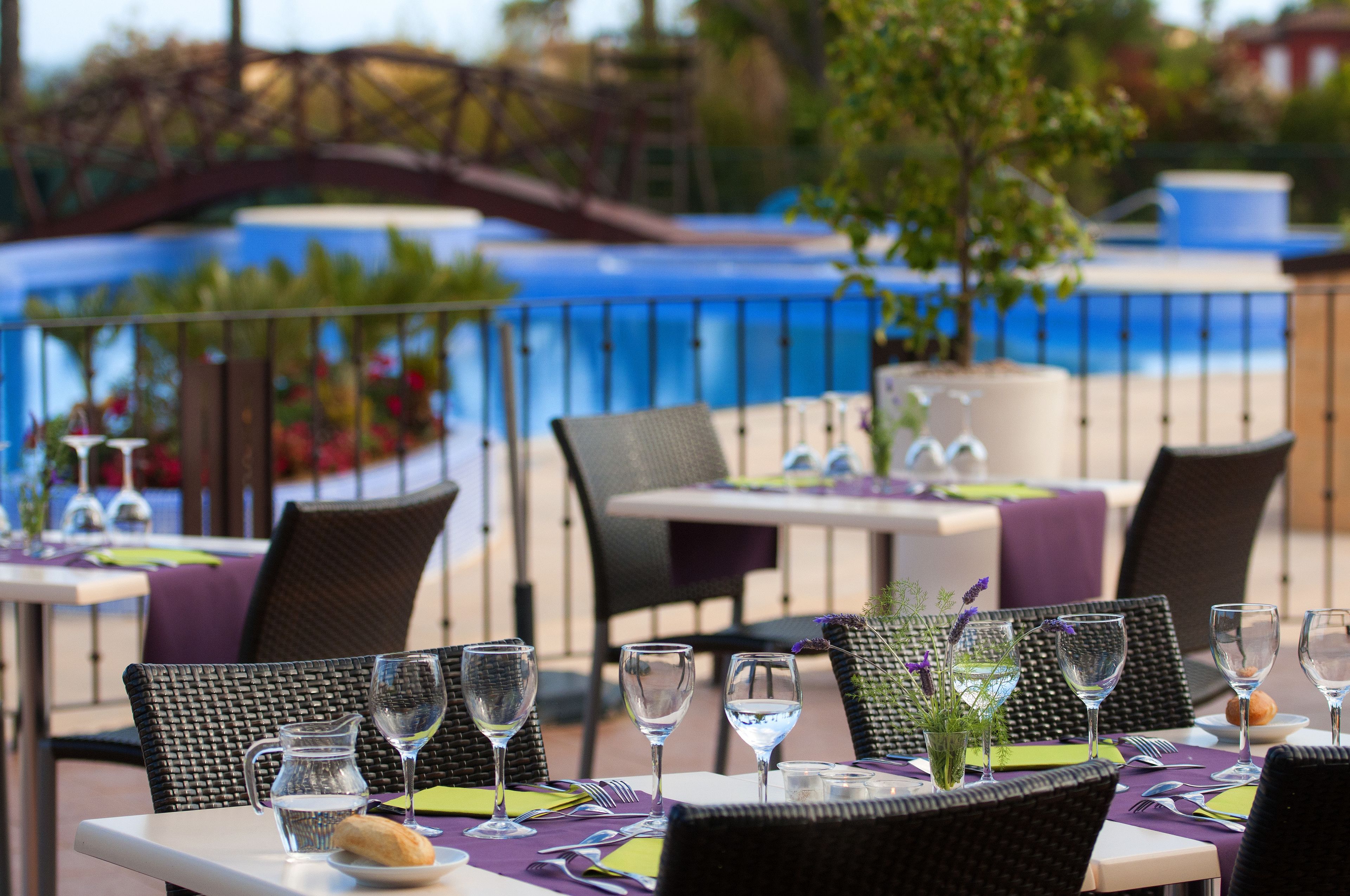 An outdoor dining area with tables set for two, each with a pitcher of water, wine glasses, and a loaf of bread.