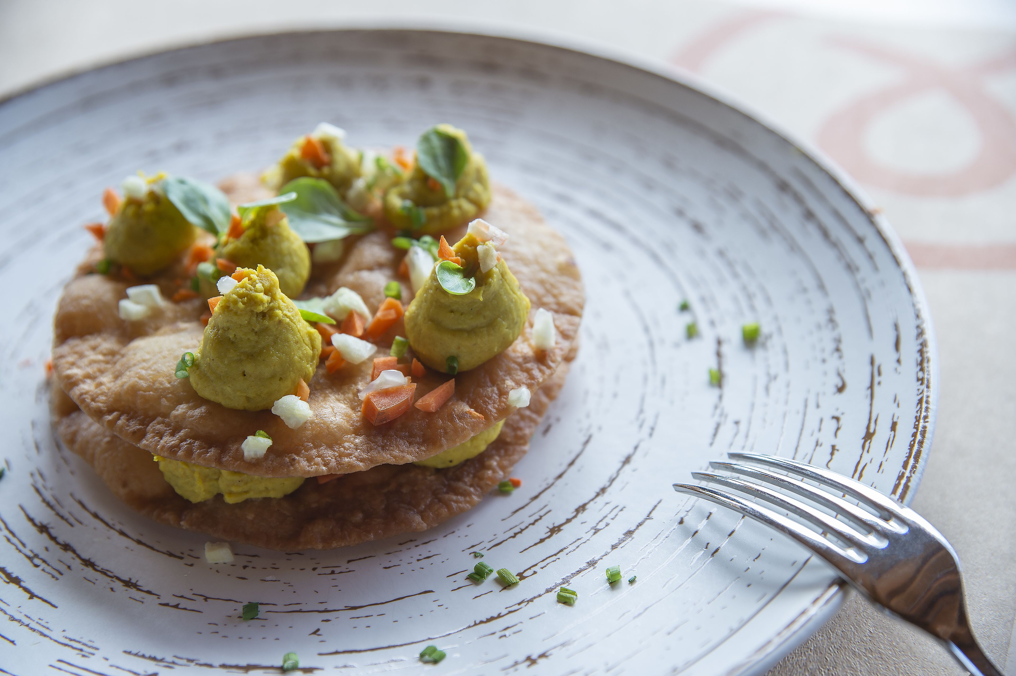 Un plato con un alimento, adornado con hierbas y pequeños vegetales, sobre una vajilla texturizada.