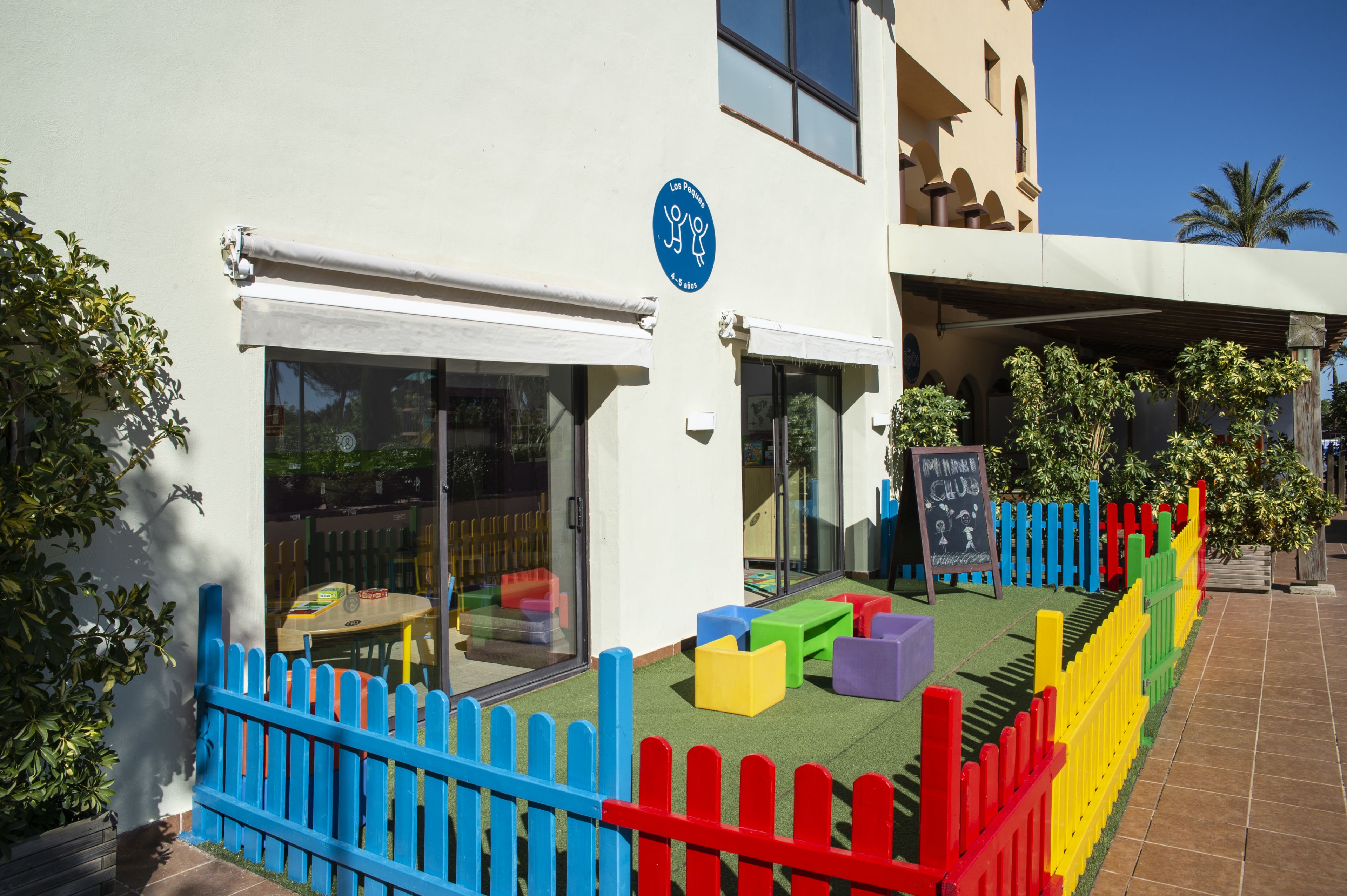 Un edificio con un área de juegos colorida, un letrero que indica un club infantil y un cielo despejado.
