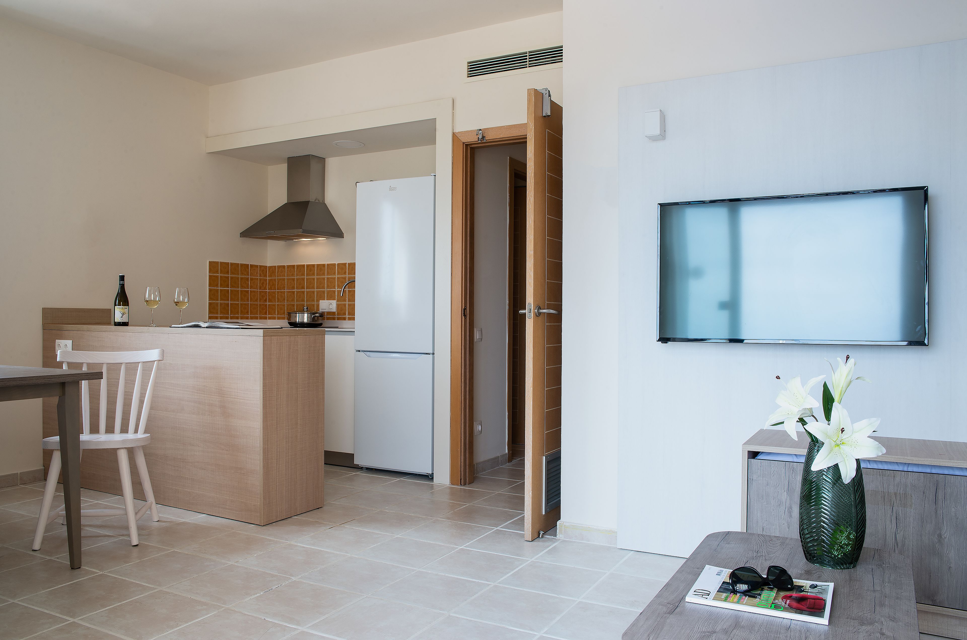 Une cuisine moderne avec un coin repas, un téléviseur fixé au mur et un vase rempli de fleurs placé sur une table d’appoint.
