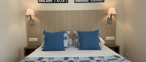 Quarto de hotel com cama, duas mesas de cabeceira, duas luminárias fixadas na parede e três quadros decorativos.