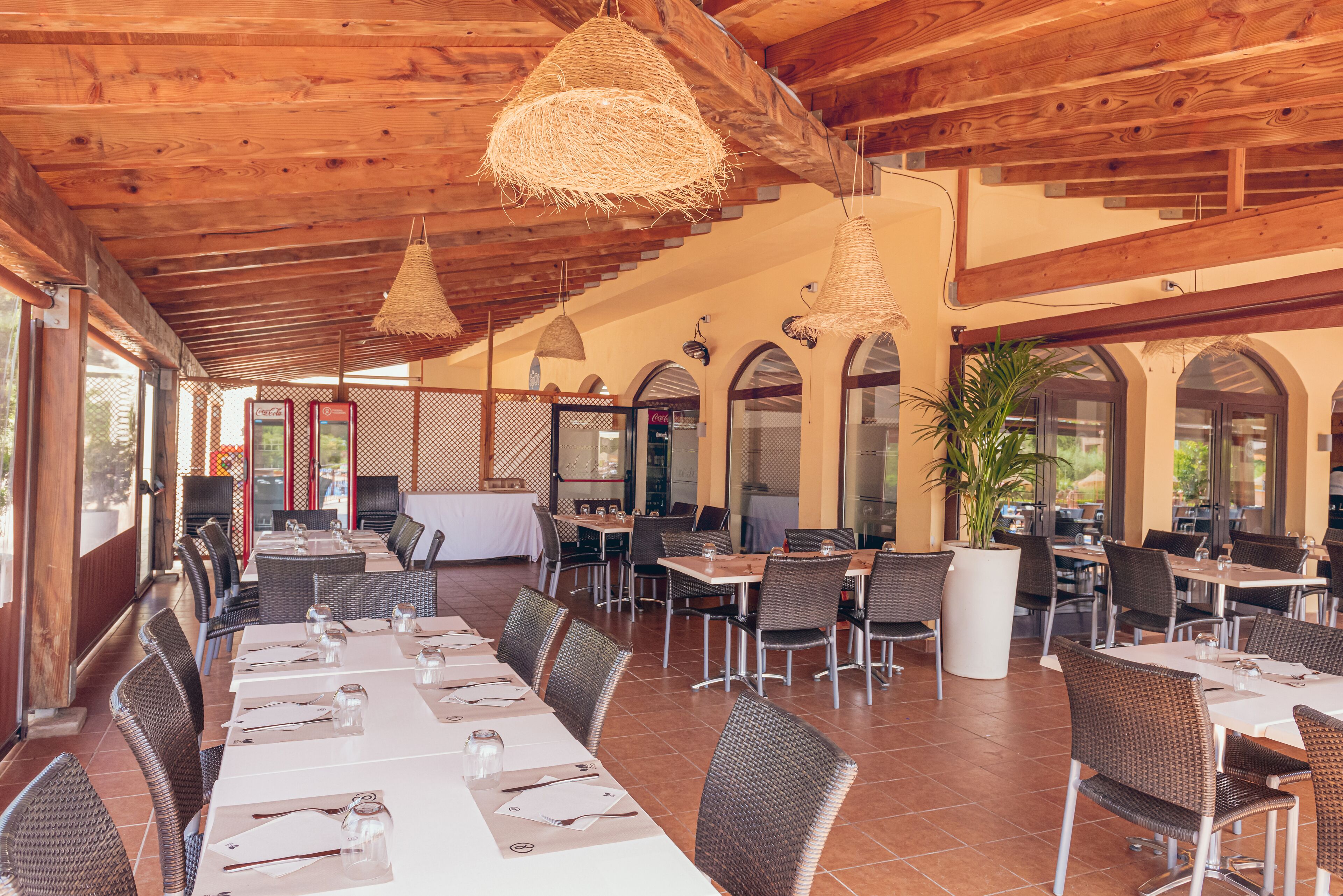 An outdoor restaurant with wooden beams, wicker furniture, and large windows.