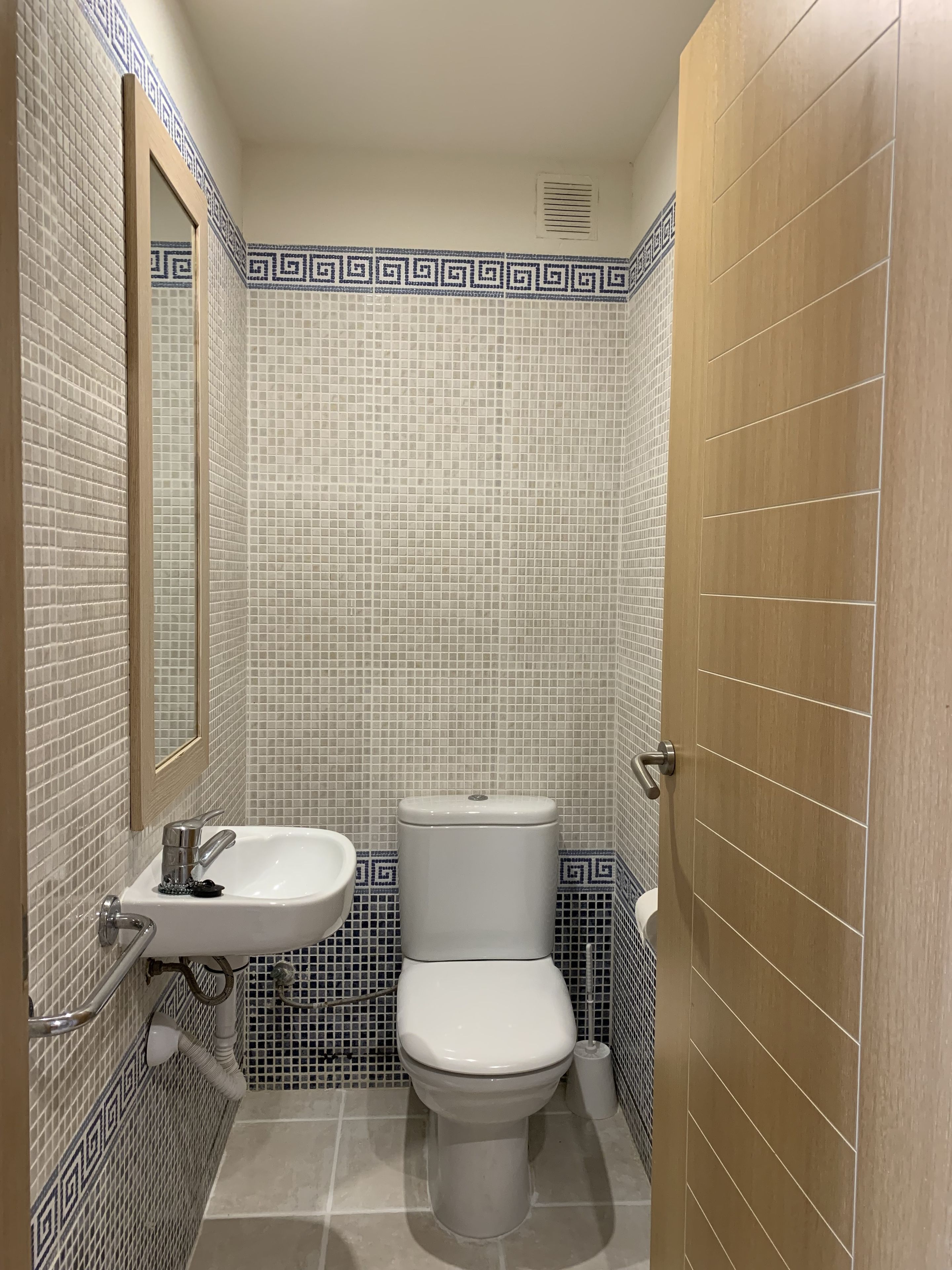 A bathroom with a white sink, a toilet, and a mirror. The walls are tiled with a blue and white pattern.