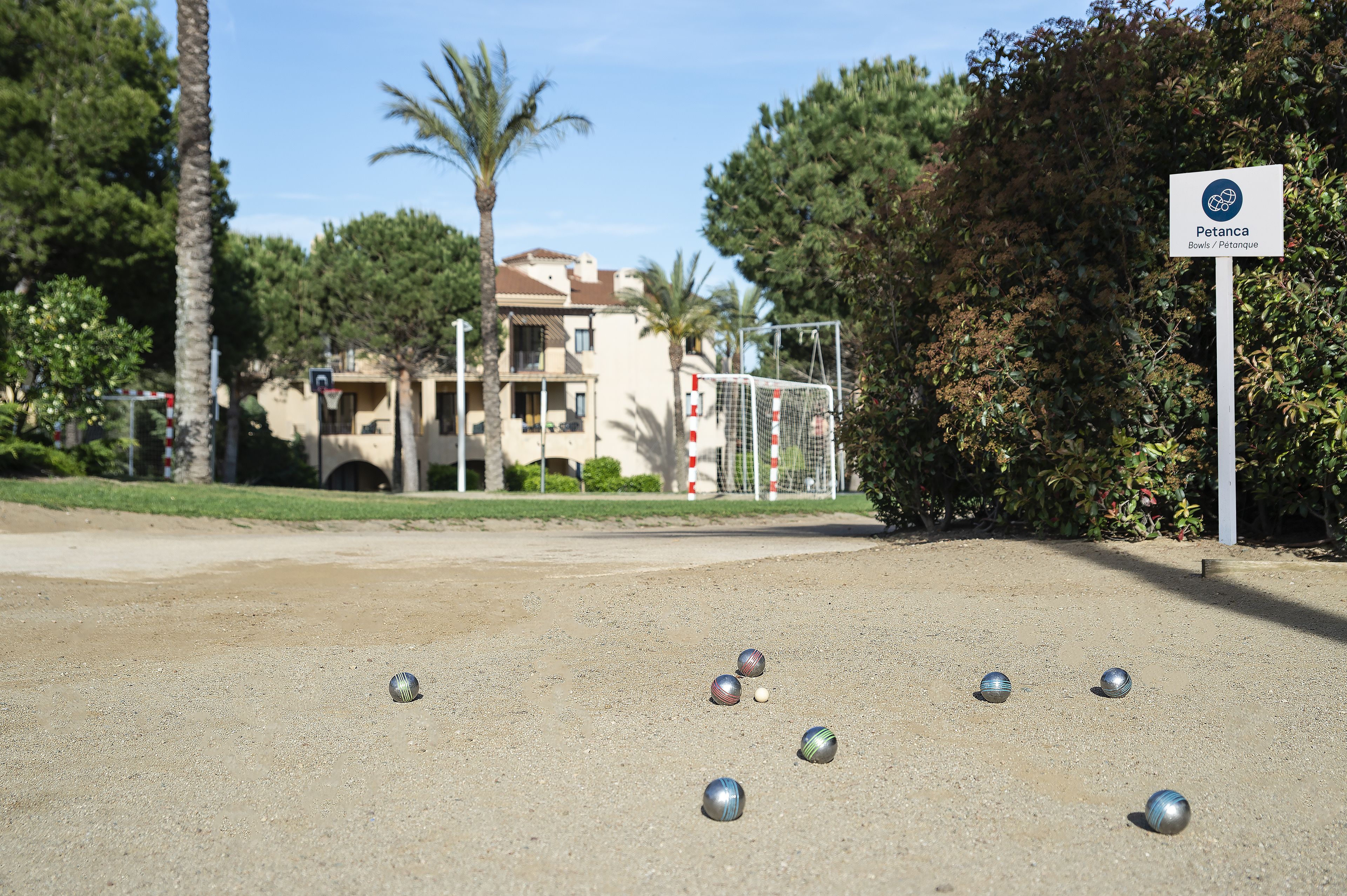 Una cancha de bochá con pelotas dispersas en el suelo, un arco de portería y un letrero que indica el lugar como Petanca.