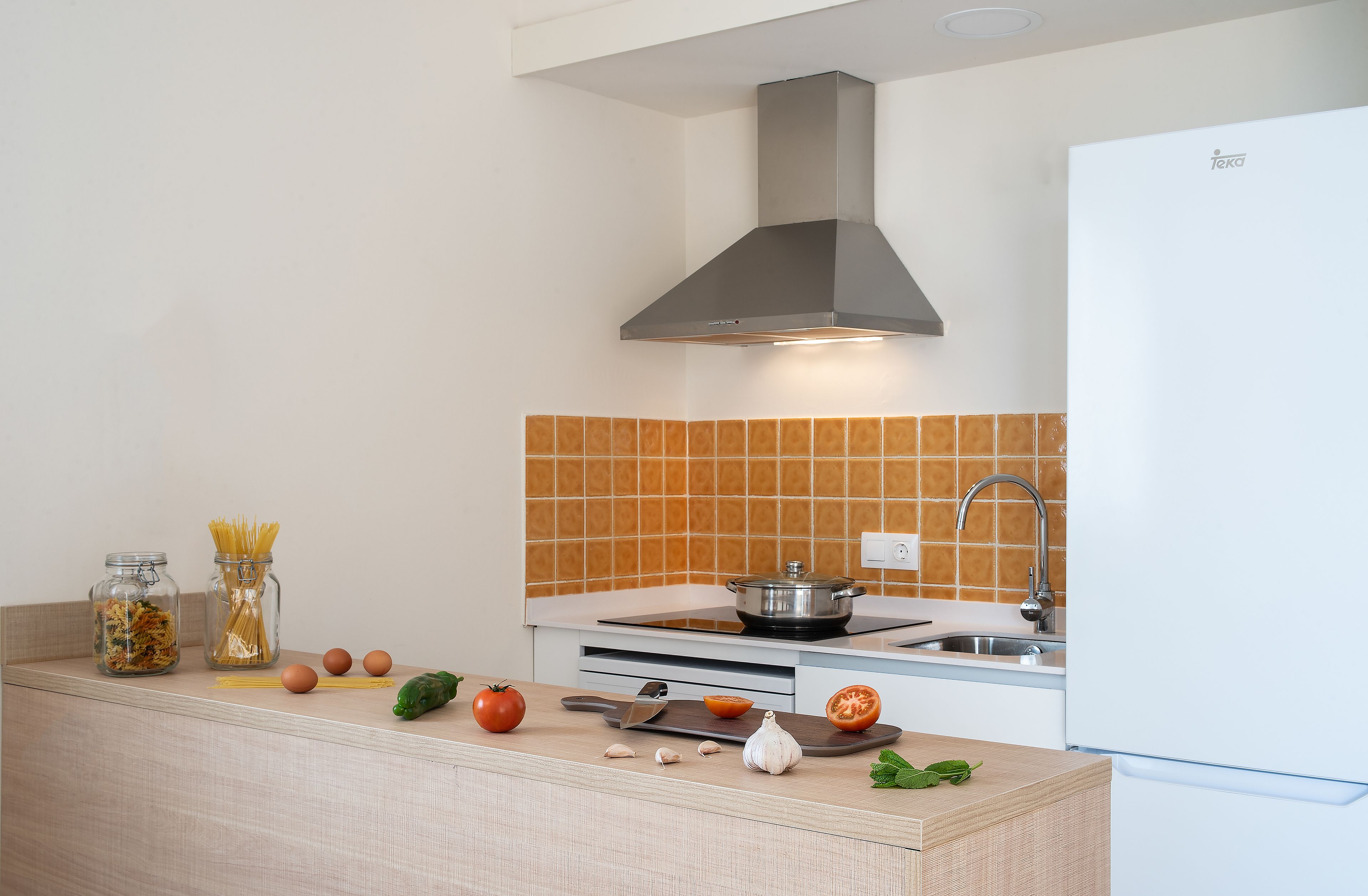 A modern kitchen with a stove, sink, and a backsplash of orange tiles.