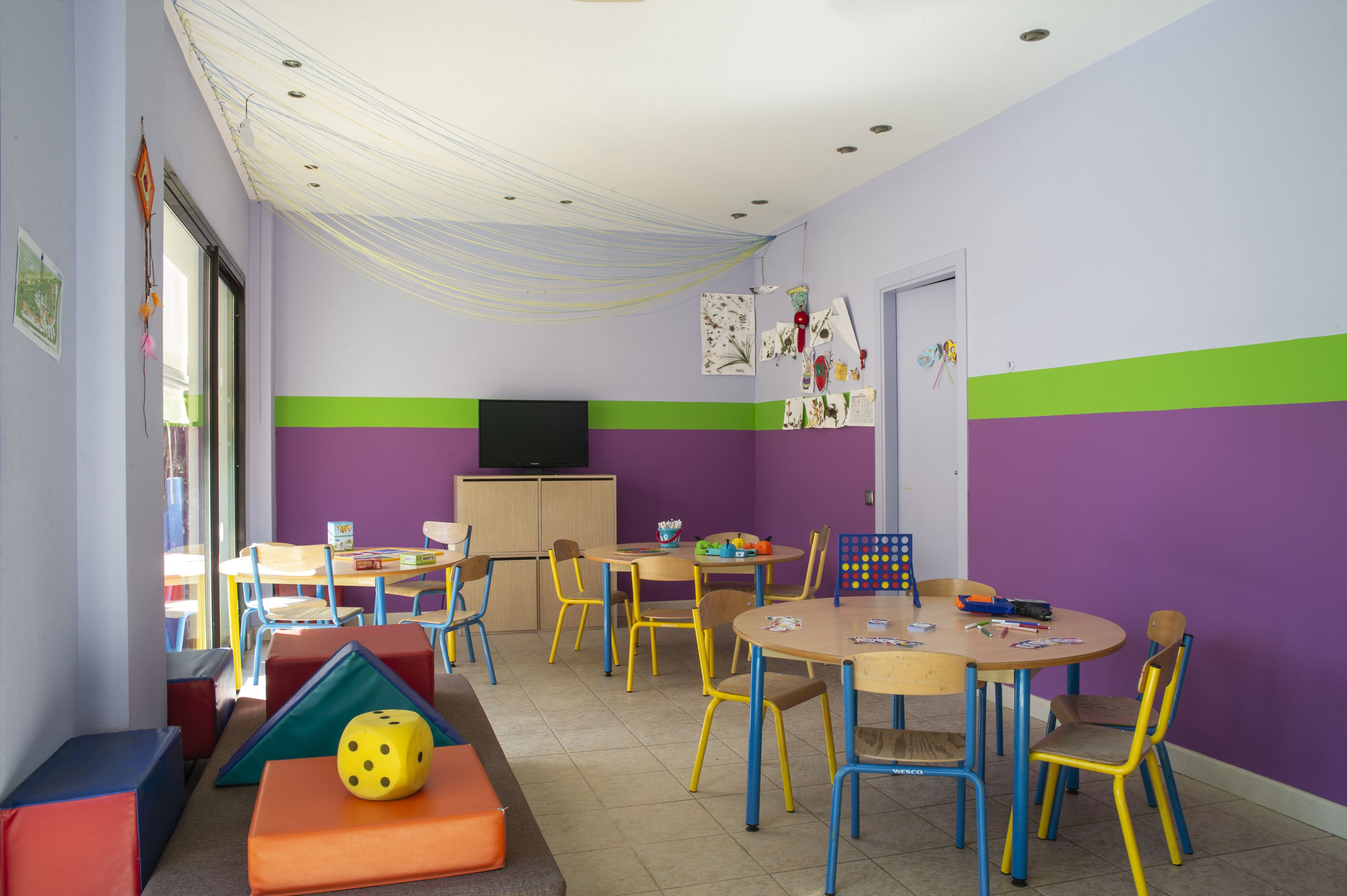 Ein Kinderzimmer mit bunten Möbeln, einem Fernseher und lehrreichen Materialien an den Wänden.
