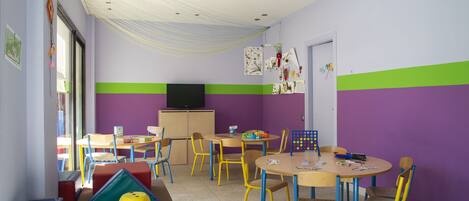 Ein Kinderzimmer mit bunten Möbeln, einem Fernseher und lehrreichen Materialien an den Wänden.