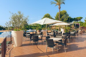 An outdoor patio with tables and chairs, a pool, and a palm tree.