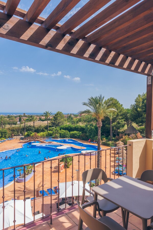 A pool area with multiple swimming pools, a covered seating area with tables and chairs, and a view of the surrounding landscape.