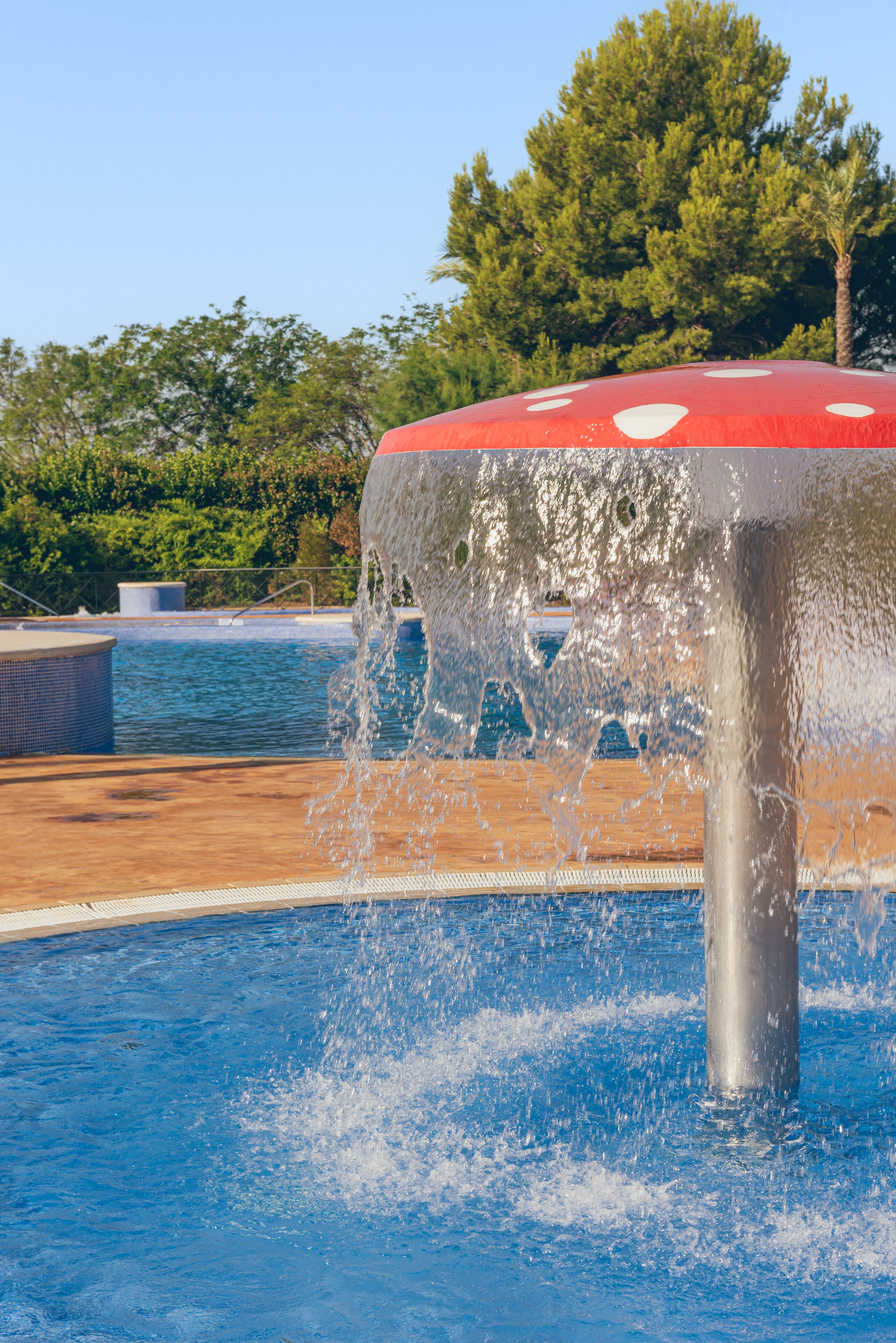A pool with a water feature, surrounded by a wooden deck and trees.