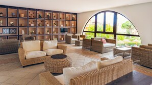 A spacious lounge area with wicker furniture, a large arched window, and a wall of shelves with decorative items. - Pierre & Vacances Resort Bonavista de Bonmont (Mont-roig del Camp)