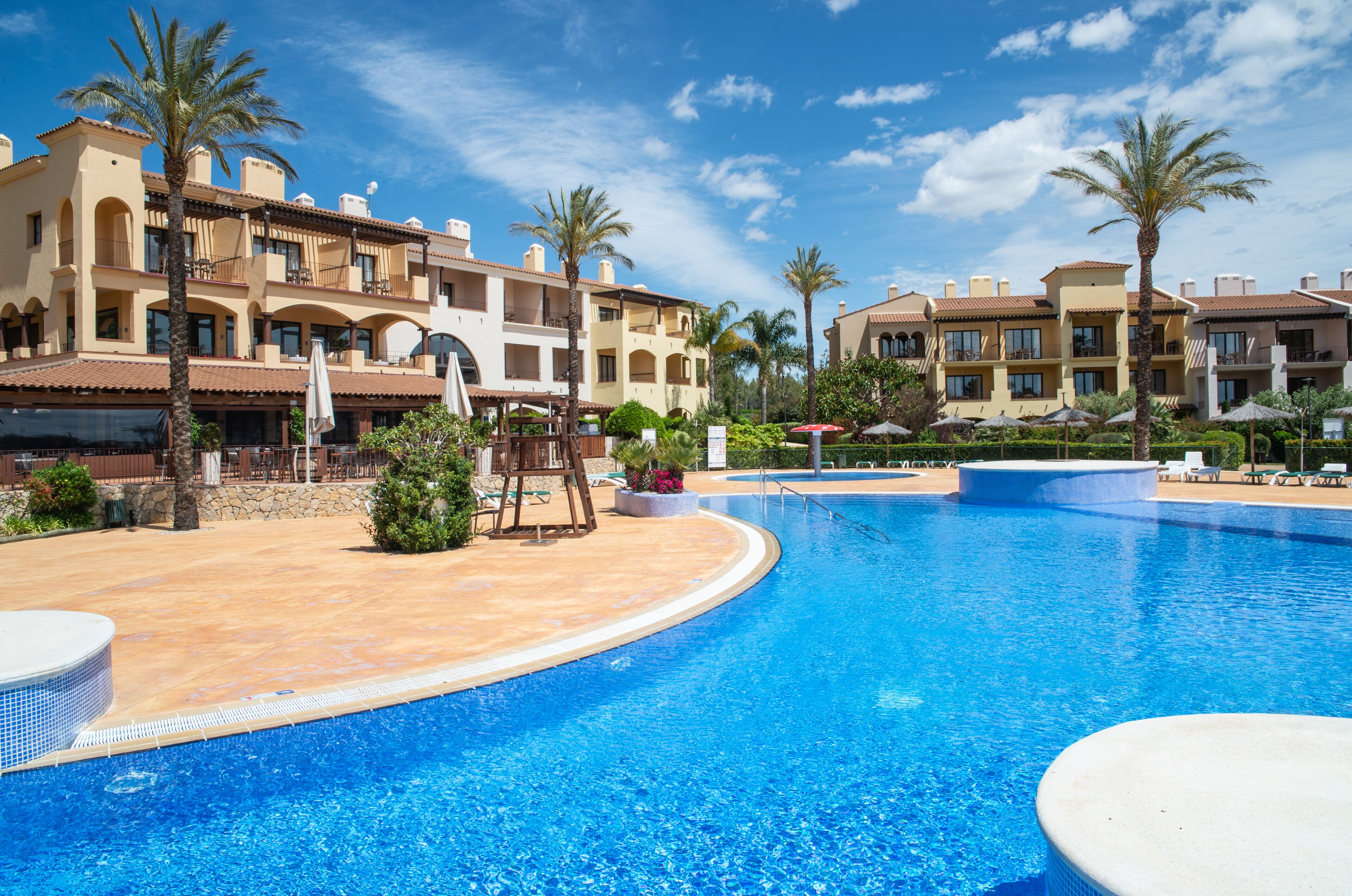 Ein Hotel mit Swimmingpool, Palmen und wolkenlosem, blauem Himmel.