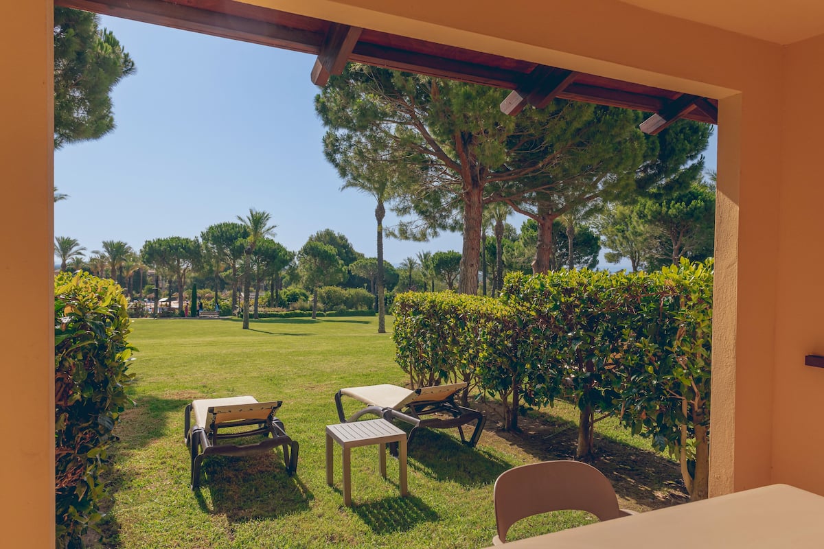 An outdoor patio with a table and chairs, surrounded by greenery and trees.