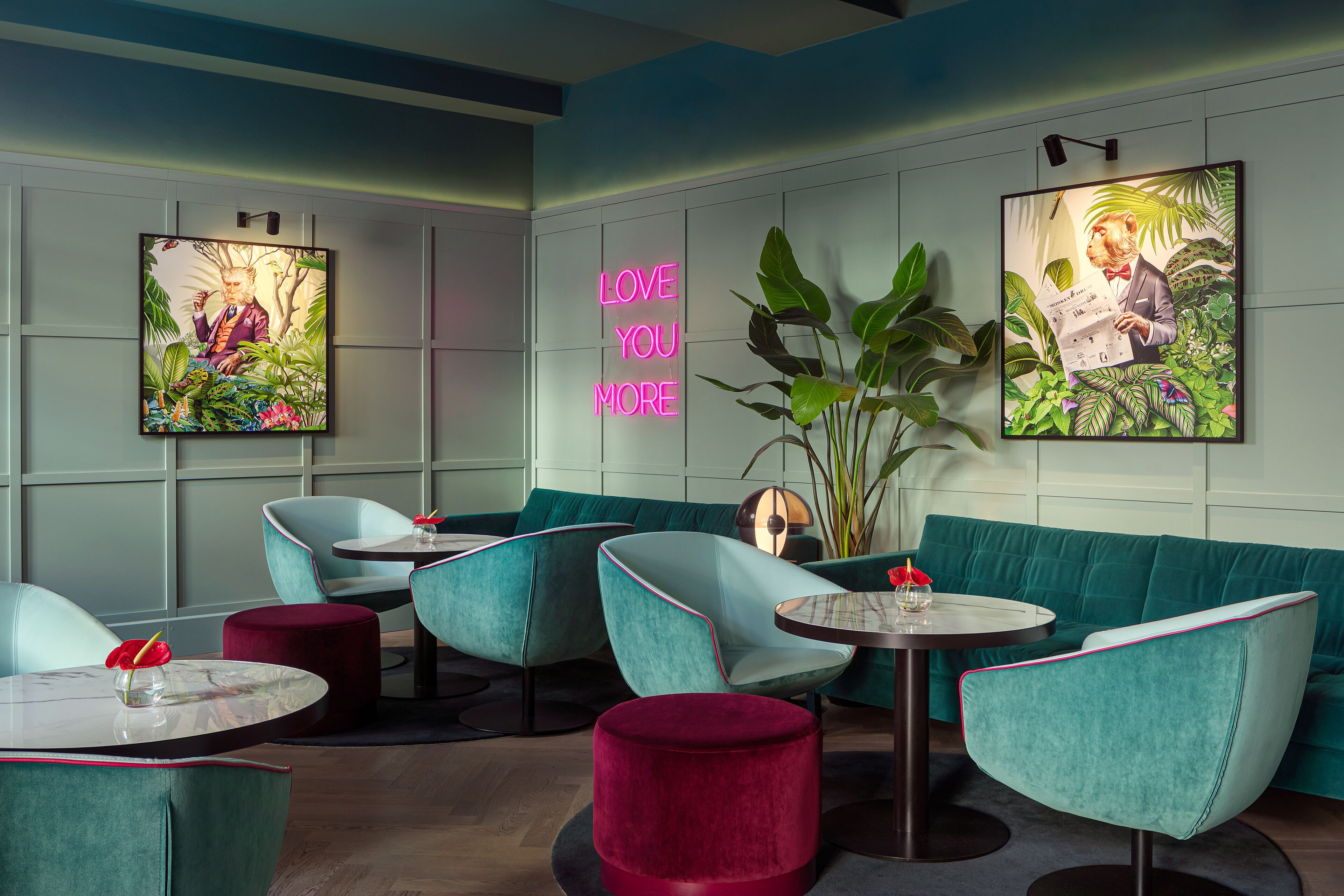 Ein moderner Lounge-Bereich mit sesshaften Möbeln in Türkis, einem Neon-Schild mit der Aufschrift 'LOVE YOU MORE' und Kunstwerken an den Wänden.