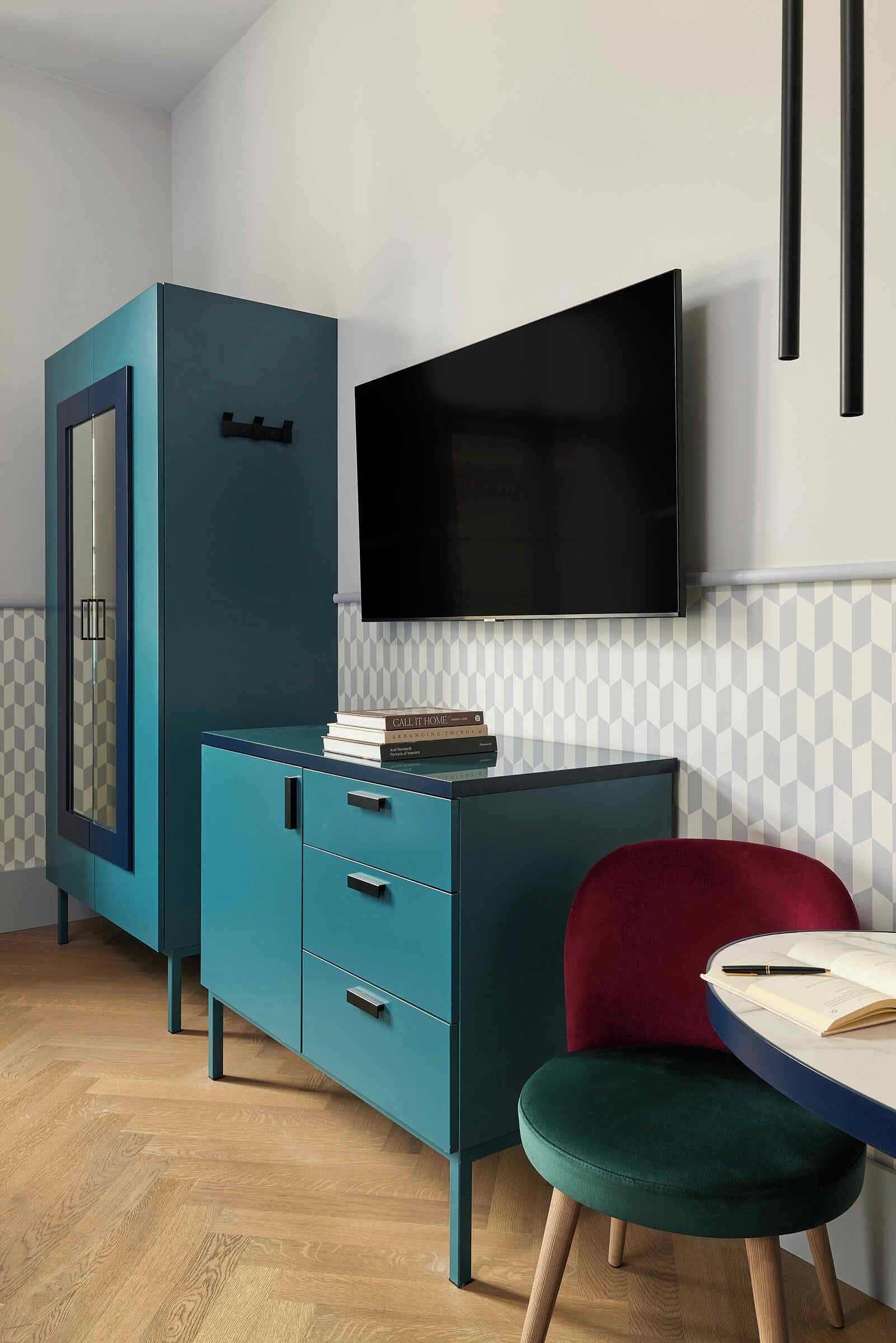 Una habitación moderna con un mueble de color verde azulado, una silla roja y un televisor de pantalla plana en la pared.