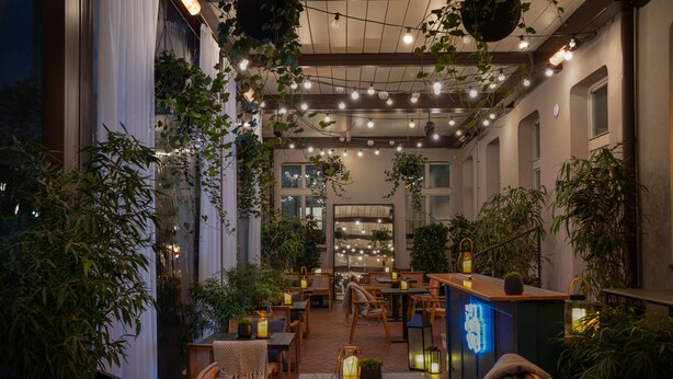 An indoor patio area with tables and chairs, string lights, and hanging plants. - Falkensteiner Hotel Prague (Prague)