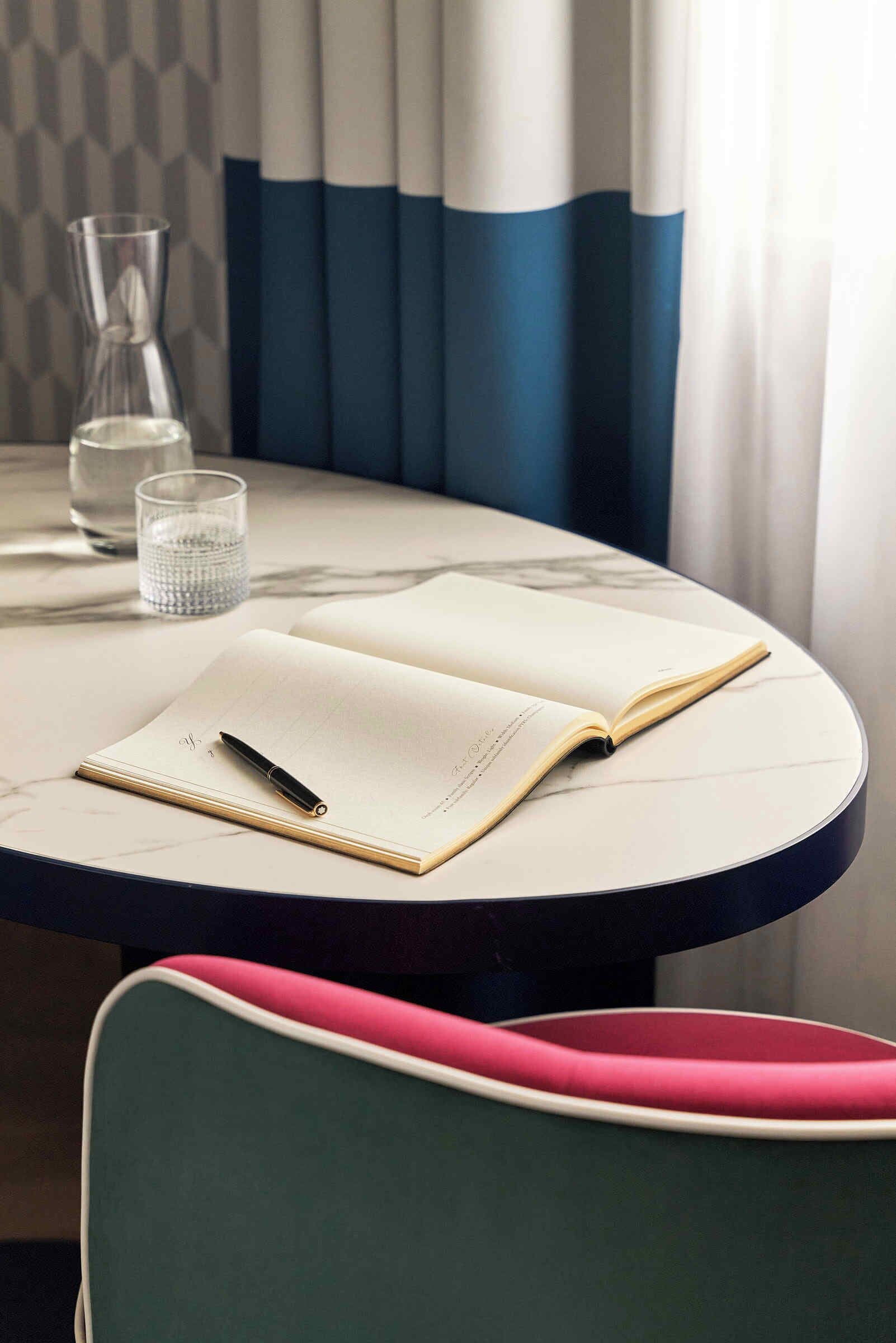 Una mesa redonda con un cuaderno, bolígrafo y un vaso de agua.